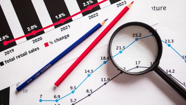 colored pencils and a magnifying glass over documents with graphs